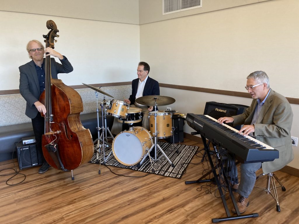 This is a photo of a jazz trio, consisting of string bass, drum set and a keyboard.